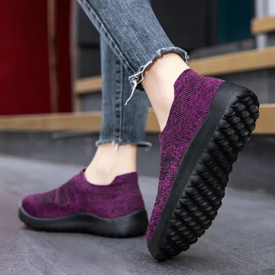 Casual Flyknit slip-on sneakers in purple, showcasing a breathable design and comfortable fit on a person's foot.