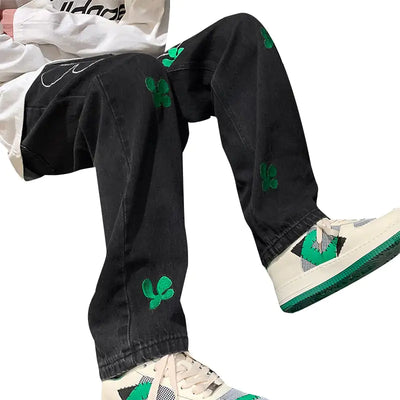 Men's embroidered high street jeans in black with green floral details, paired with stylish white sneakers.